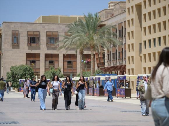 Males and females are walking in an open space. There are buildings around them