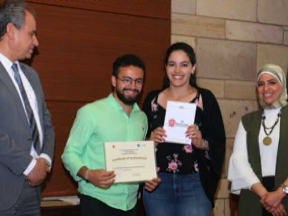 A male and a female are holding certificates. They are standing with AUC Provost Ehab Abdel Rahman