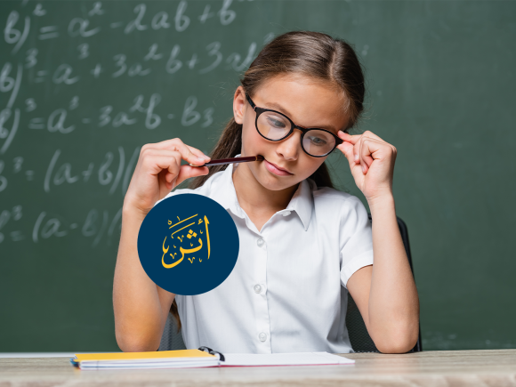 ِA girl is wearing glasses and holding a pencil in her mouth. There is a blackboard behind her with mathematical figures. Text: أثر