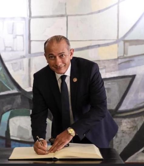 A man smiling and appears to be signing in a book