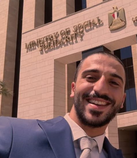 A male is smiling in front of a building with the text: Ministry of Social Solidarity