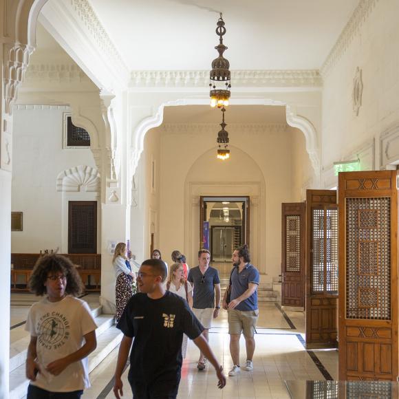 Students walking in a corridor with Islamic wooden doors and chandeliers