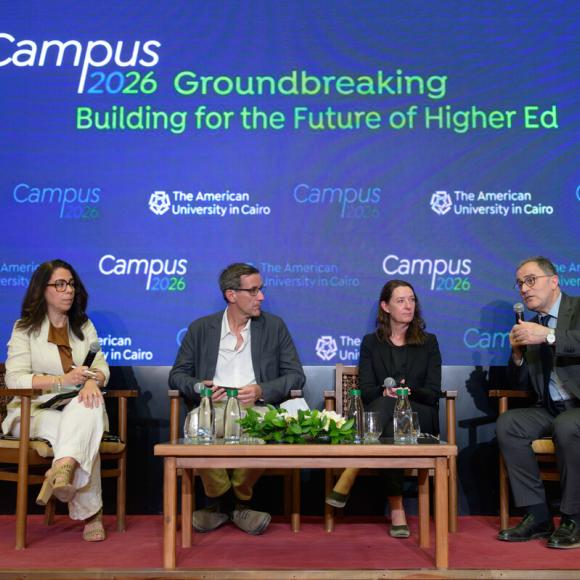 Two men and two women sitting at a podium. One of the men is talking into a microphone. Text: Campus 2026 Groundbreaking. Building for the Future of Higher Ed. The American University in Cairo