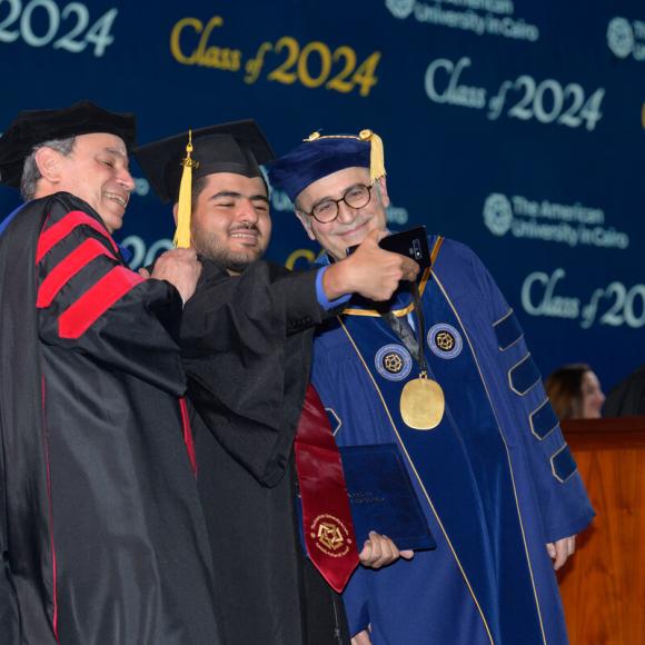 Three males are taking a selfie together, they are dressed in caps and gowns. Text: The American University in Cairo. Class 0f 2024