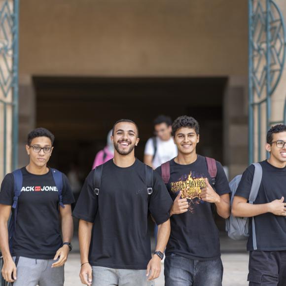 four male students wearing black tshrits and jeans walking on campus