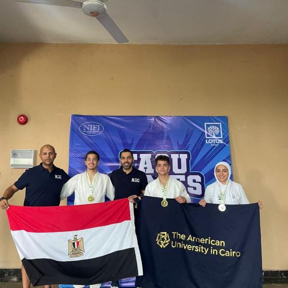 Two males standing with three athletes who are wearing medals and holding the Egyptian flag and The American University in Cairo 