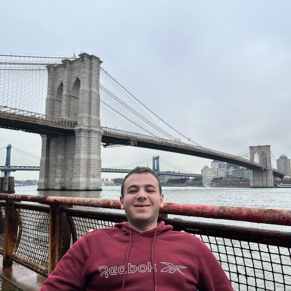 A male is sitting in front of a Brooklyn Bridge in New York