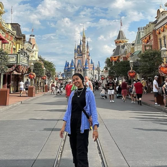 A female student is standing in front of the Disney Castle