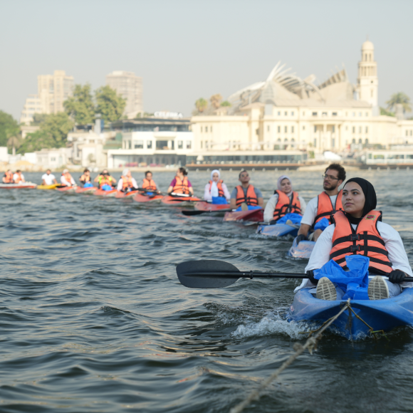 A group of students, each in a boat on the Nile, kayaking in a line one after the other and picking up waste from the Nile