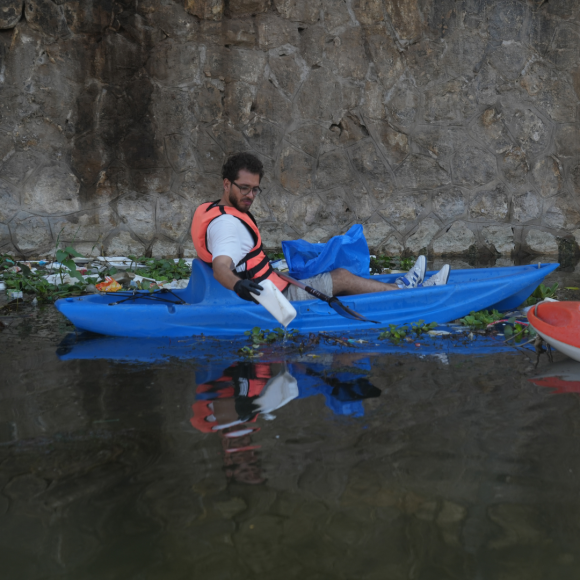 A male student on a boat in the Nile picking up a plastic cup from the Nile