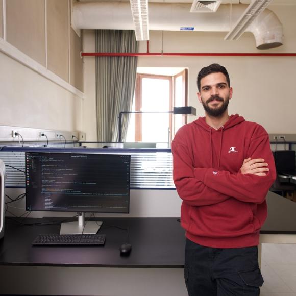 Amale is standing inside a lab, he is smiling