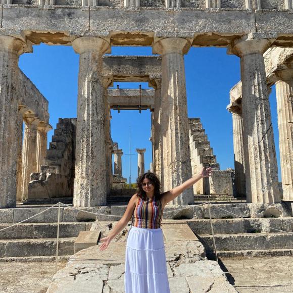 A female is standing in front of ancient pillars in Greece